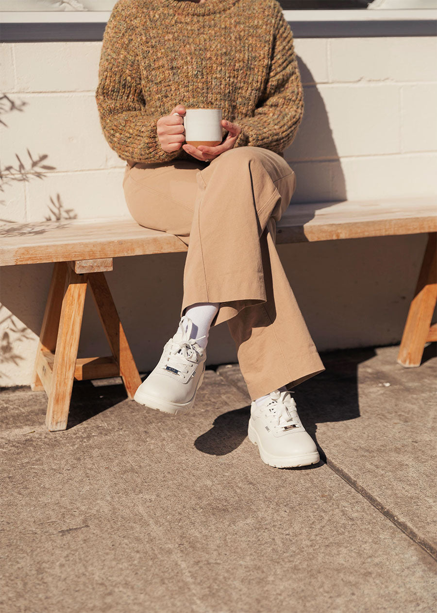 woman with a coffee in white sneakers that are a wide fit