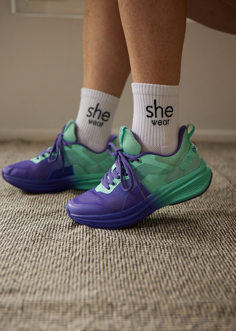 Interior shot of woman's feet in white cooldry sports socks and purple and aqua walking sneakers with purple laces.