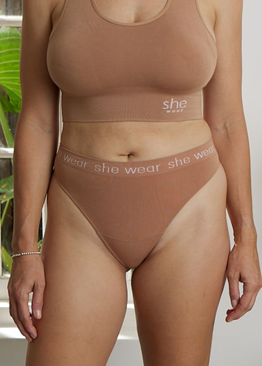 Curvy woman by a window wearing comfortable, stretchy organic bamboo underwear and crop top bra in nude or beige flesh tone.