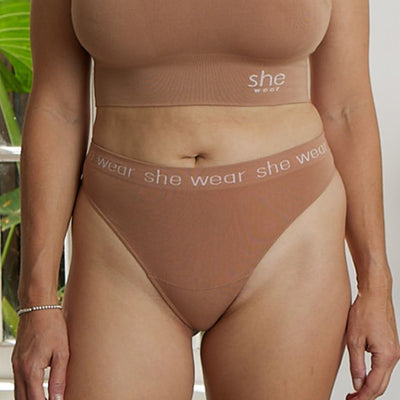 Curvy woman by a window wearing comfortable, stretchy organic bamboo underwear and crop top bra in nude or beige flesh tone.